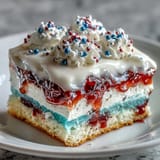 Festive red, white, and blue Patriotic Poke Cake glistening with white chocolate ganache.