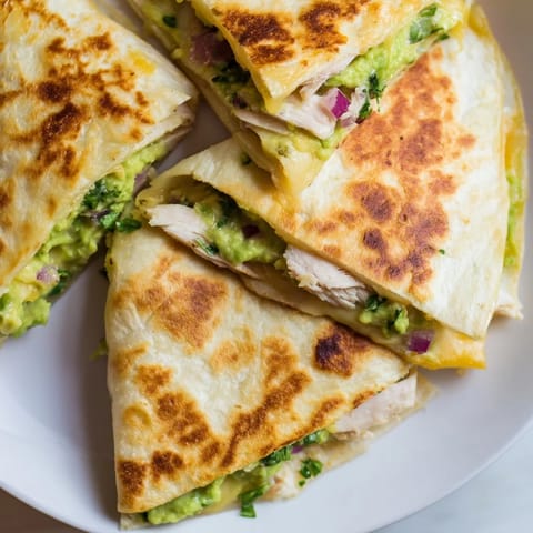 A close-up of Chicken Avocado Quesadilla slices arranged on a plate, topped with fresh cilantro and lime wedges.