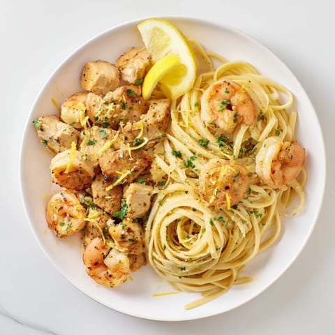 A vibrant plate of Lemon Garlic Shrimp & Chicken Pasta with juicy shrimp and tender chicken pieces, drizzled with a glossy lemon-garlic butter sauce.