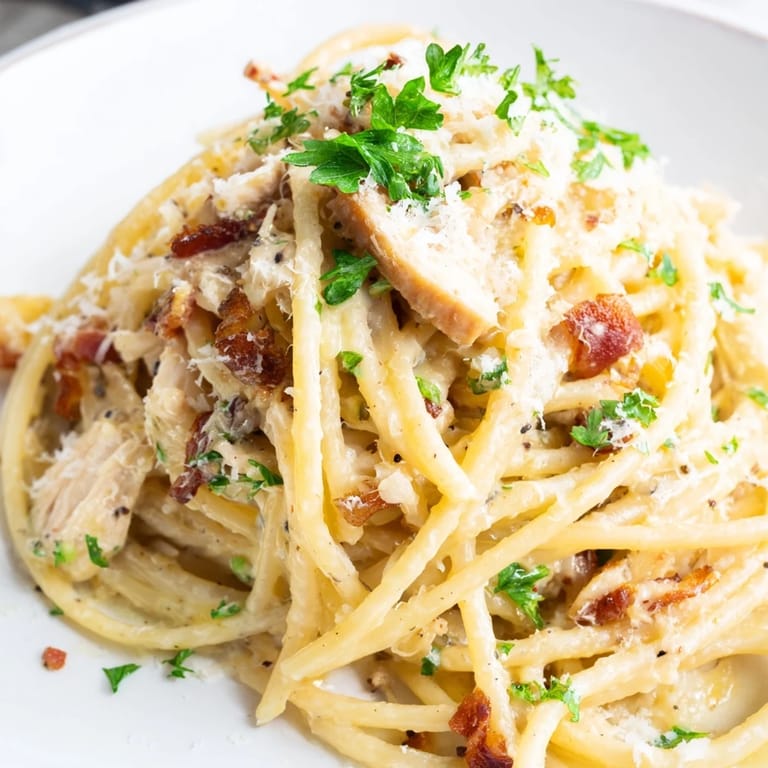 Savory chicken carbonara served in a white bowl, garnished with chopped parsley and extra Parmesan, ready for a comforting dinner.