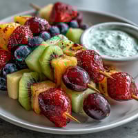 Vibrant rainbow fruit skewers featuring strawberries, pineapple, kiwi, and grapes served with creamy honey-yogurt dip for a refreshing summer snack.