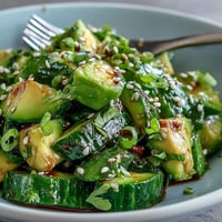 Vibrant smashed cucumber and avocado salad with sesame dressing, garnished with green onions and sesame seeds for a fresh, healthy meal.